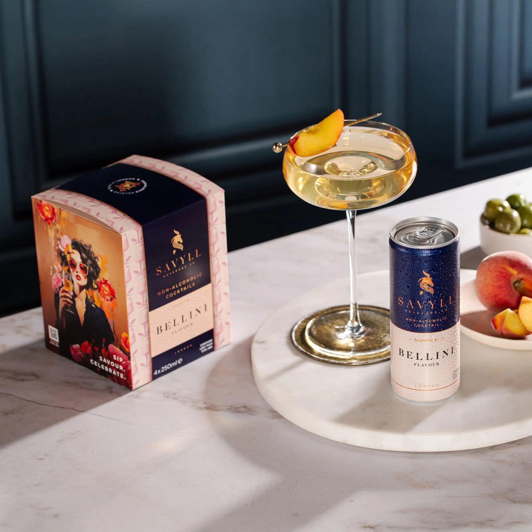 Savyll alcohol-free Bellini 4-pack box with a can, a cocktail glass garnished with peach slice, and fresh peaches on a marble surface.
