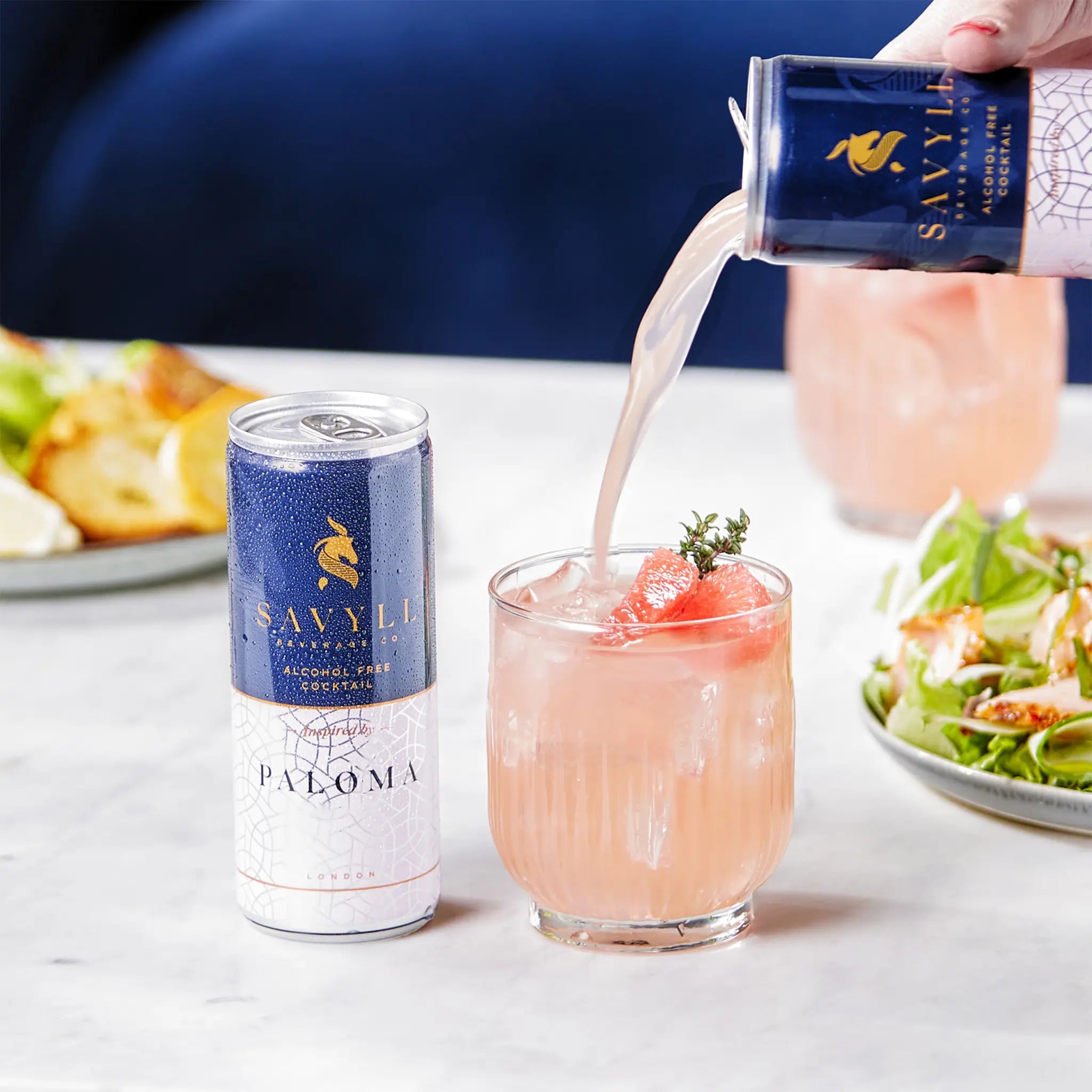 Can of Savyll non-alcoholic Paloma cocktail being poured into a glass with ice and grapefruit garnish.